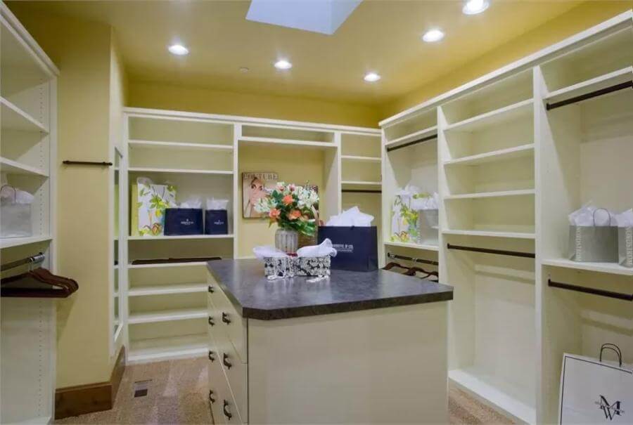 A spacious primary walk-in closet featuring white built-ins and a center island.