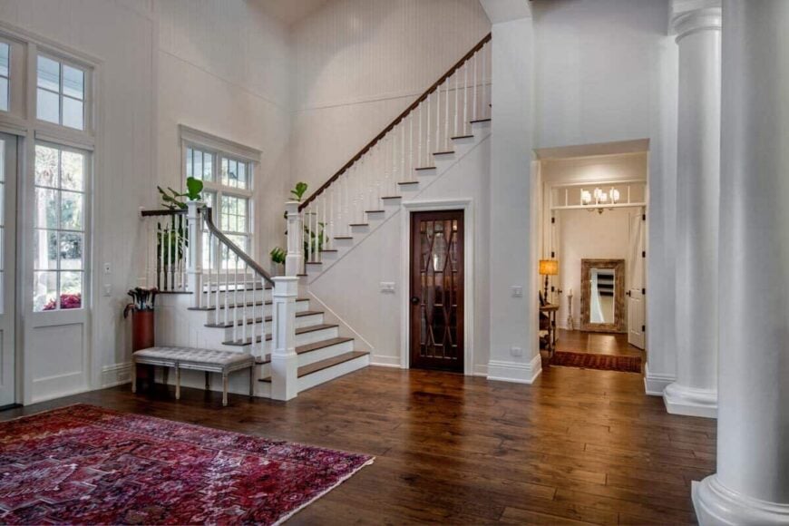 Foyer showcasing a wooden staircase, a cozy bench, and a large area rug over hardwood floors.