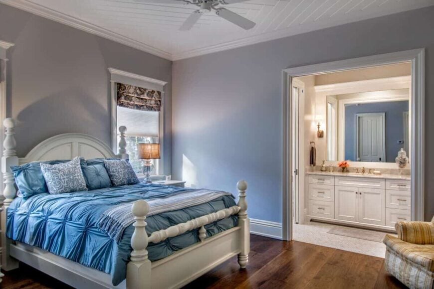 Warm bedroom featuring a white bed, a striped chair, and its own bathroom.