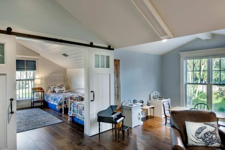 Children's bedroom revealed by sliding barn doors, furnished with metal beds.