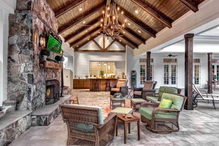 Outdoor cabana with fireplace, comfortable furniture, and wooden chandelier beneath a high ceiling.