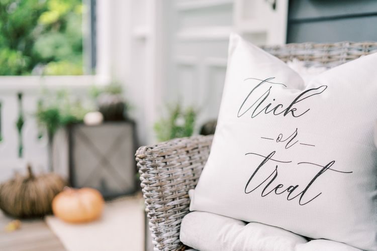Trick or treat pillow on a wicker chair on a front porch