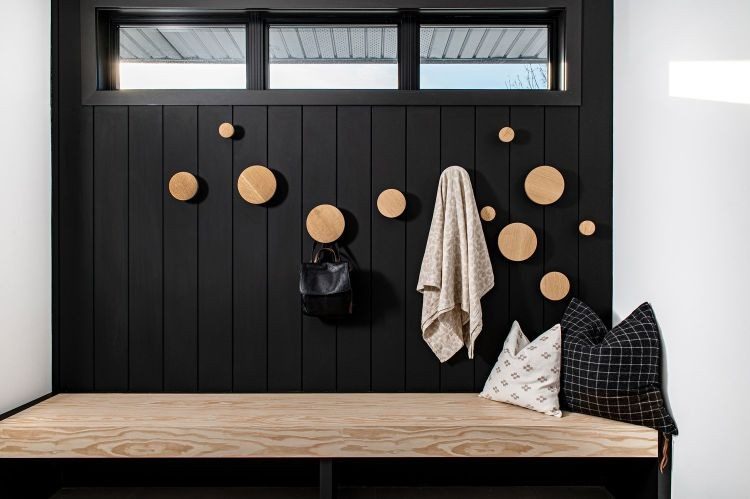 Round wooden peg hooks on a black panelled wall above a wood mudroom bench