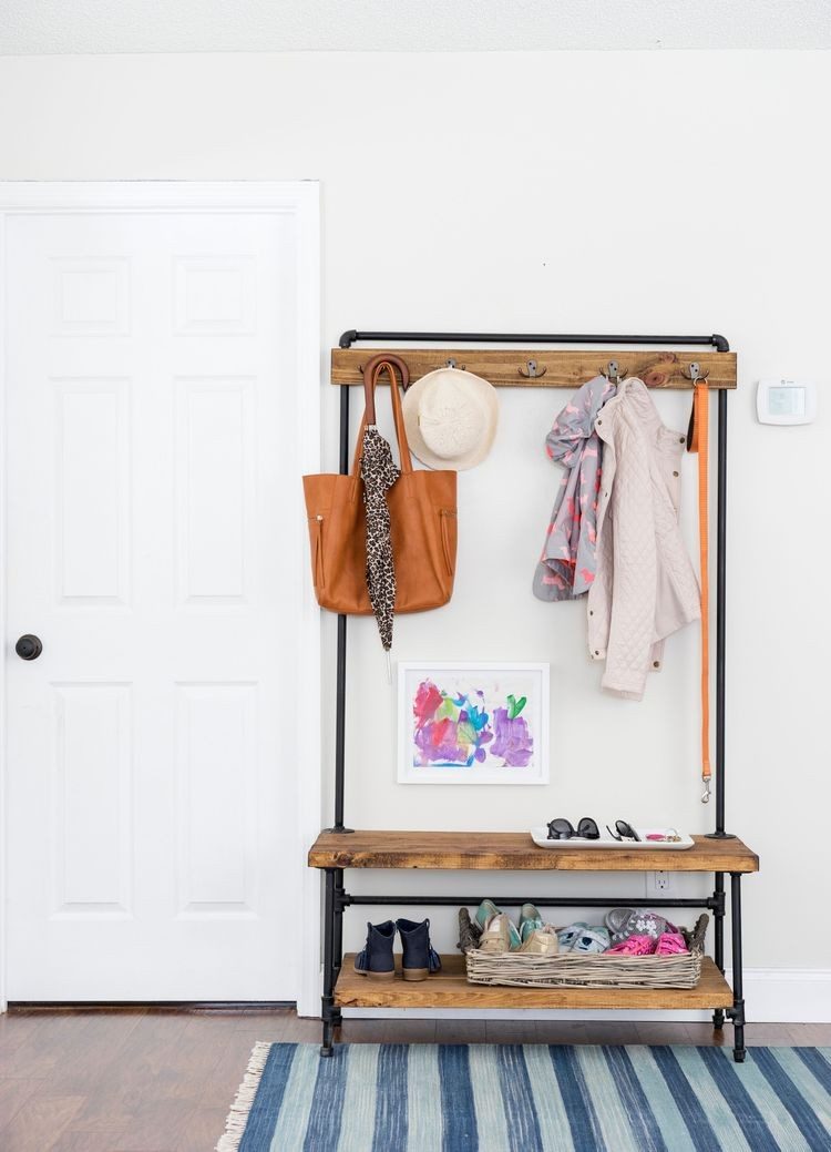 Slim freestanding coat rack with hanging bags above a small bench