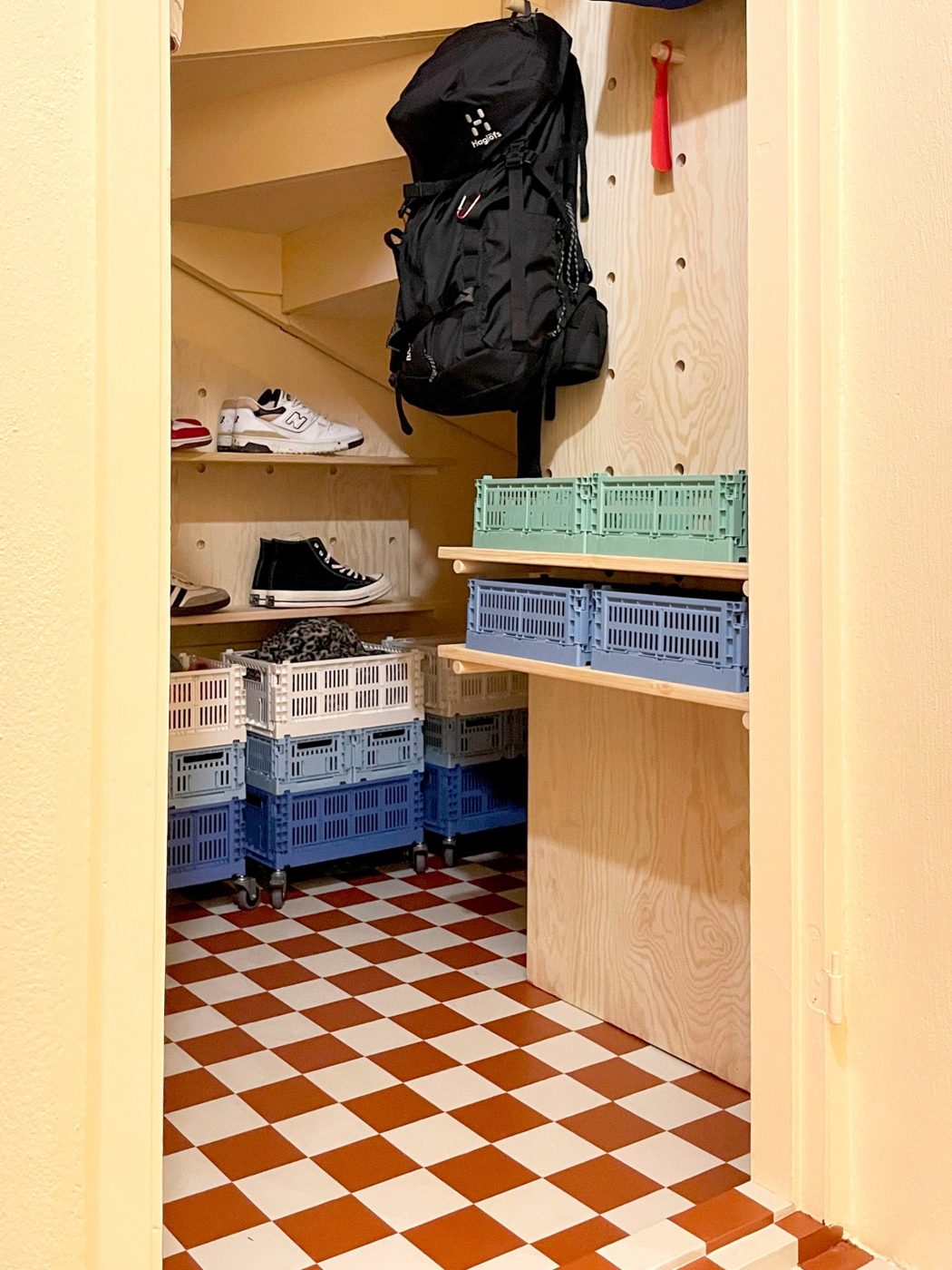 Under-stairs nook turned mini mudroom with shelves, crates and a checkered painted floor