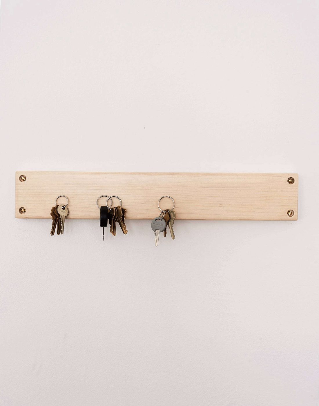 Wooden magnetic knife strip on a white wall holding sets of keys
