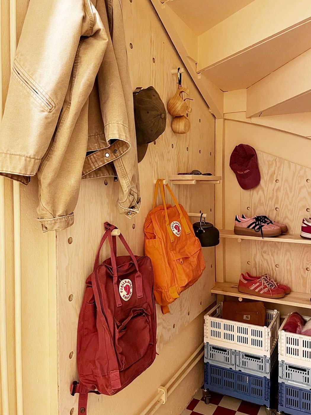 DIY plywood pegboard wall with dowels holding backpacks, caps and shoe shelves