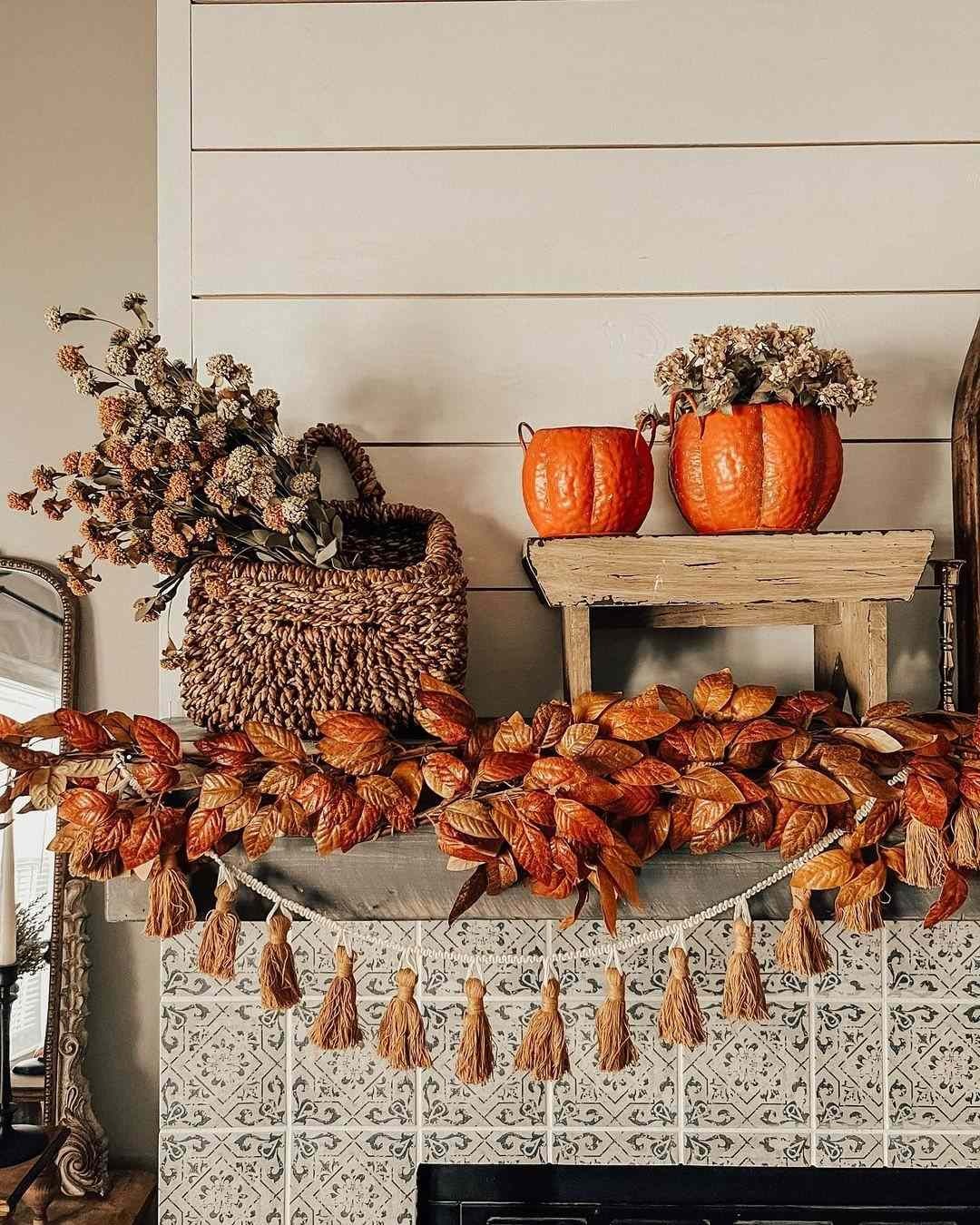 Halloween-to-Thanksgiving mantel in ochre tones with orange pumpkins, a copper leaf garland, tassel bunting and dried stems
