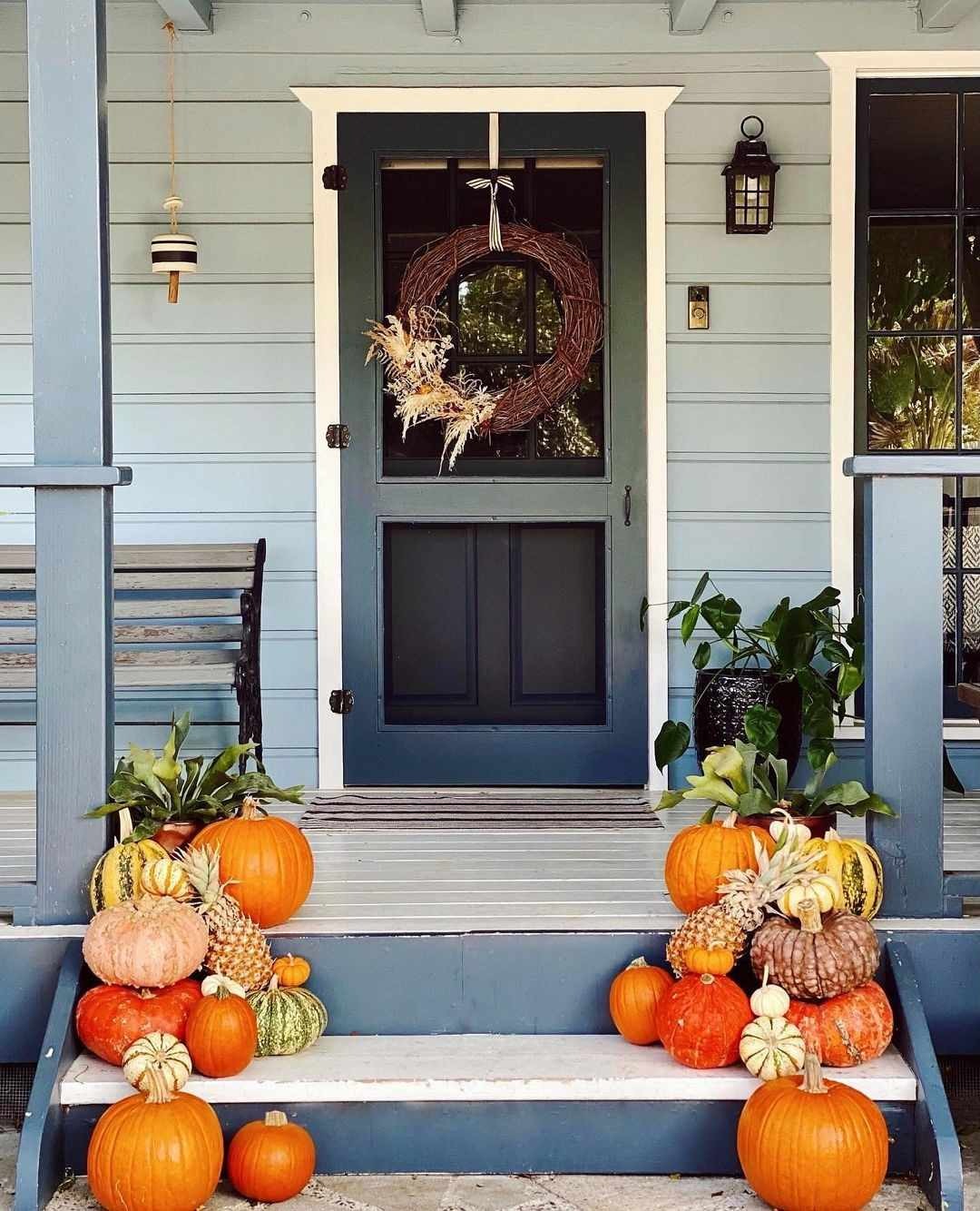 Front porch steps lined with orange, white and striped pumpkins leading to a blue front door with a fall wreath
