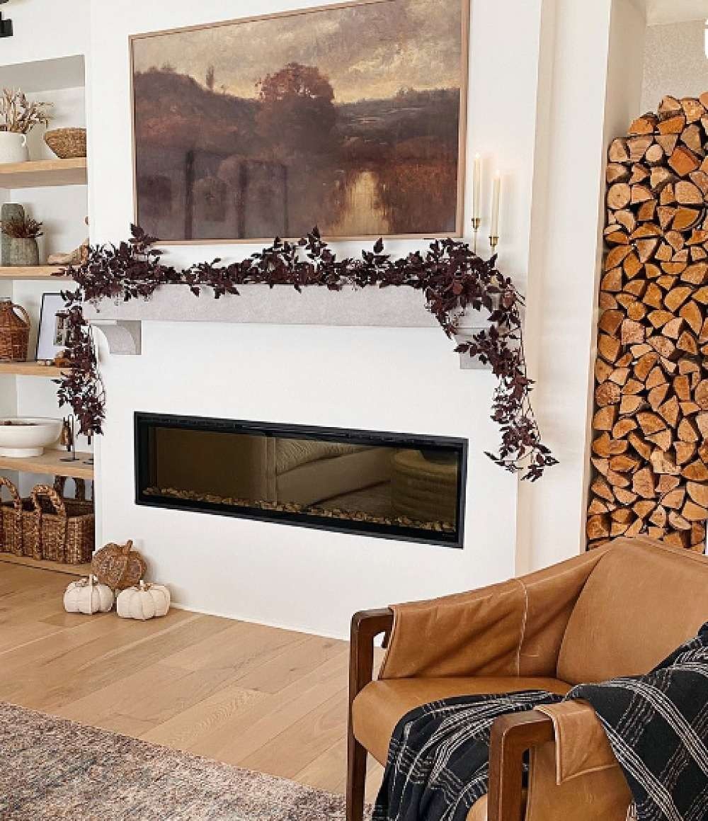 Dark dried-leaf garland draped across a white fireplace mantel beneath a moody landscape painting