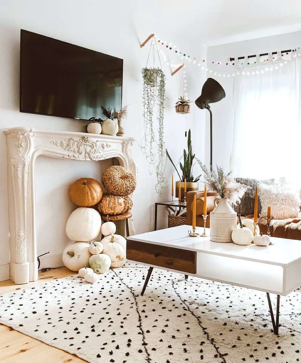 Bright living room with orange taper candles on the coffee table and white and tan pumpkins stacked in a white faux fireplace